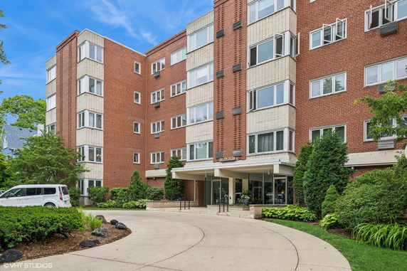 Front view of a multi-story brick apartment building with large windows and a driveway.