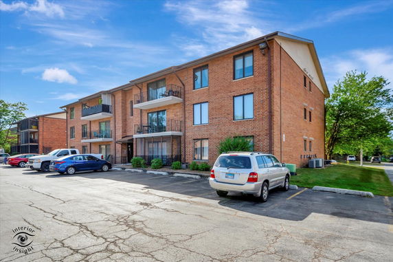 Front view of a three-story brick apartment building with balconies.