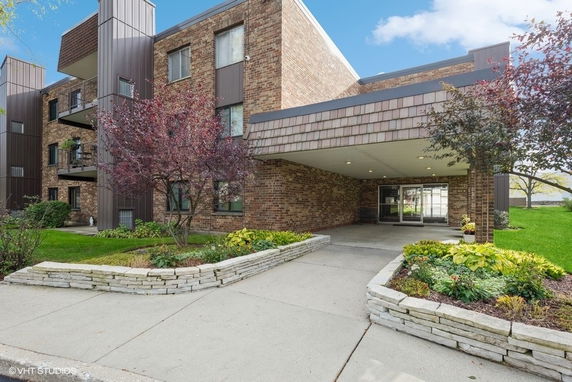 Front view of a multi-story brick building with balconies and landscaped entrance.