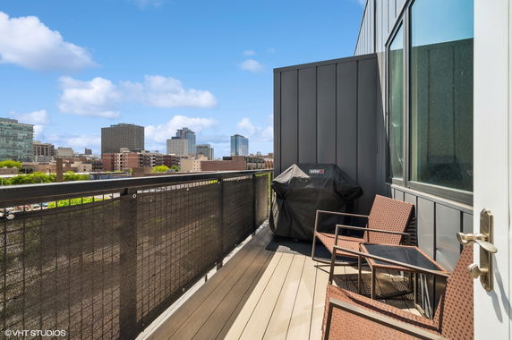 Outdoor balcony area with chairs and a barbecue grill overlooking city buildings.