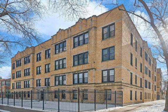 Front view of a multi-story brick apartment building with large windows and a gated entrance.