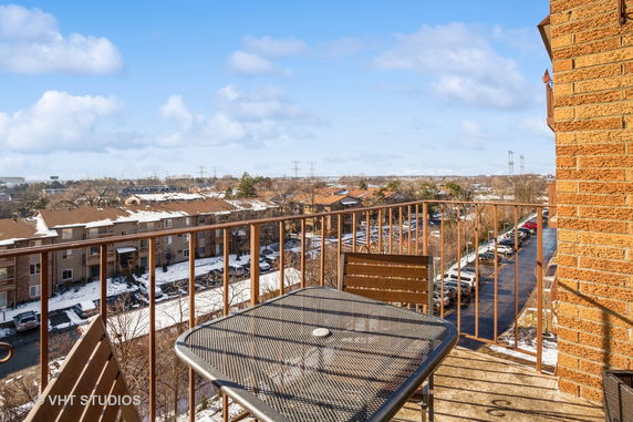 View from a balcony showing rooftops and a parking area of neighboring buildings.
