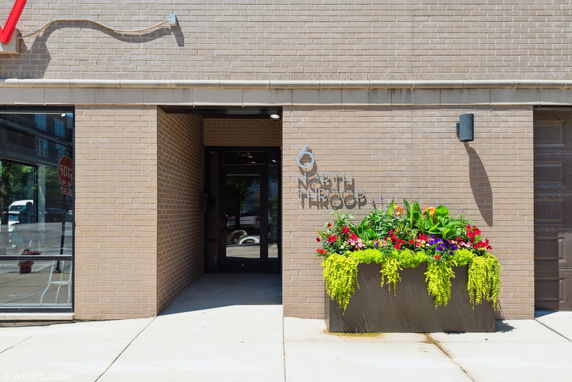 Front view of a building entrance with brick exterior and a large planter with flowers.