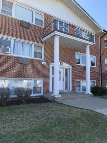 Front view of a two-story brick building with a balcony and white pillars.