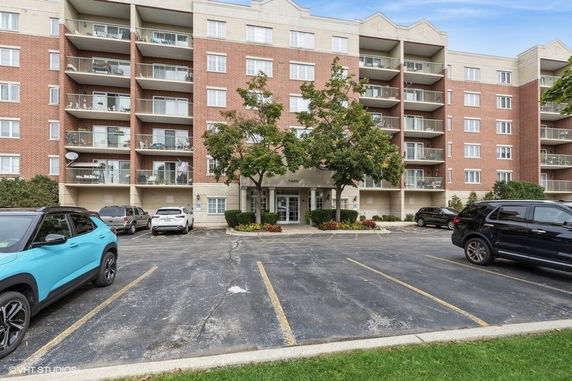 Front view of a multi-story apartment building with balconies and parking area.