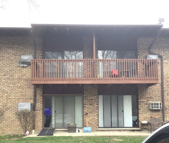 Front view of a two-story brick building with a wooden balcony and sliding glass doors.