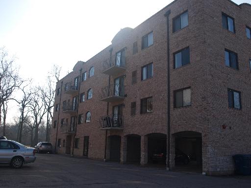 Front view of a multi-story brick building with several balconies and an open parking area below.