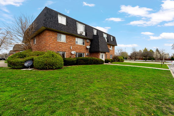 Front view of a multi-story brick building with dark roof and satellite dishes.