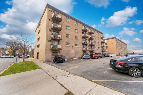 Front view of a multi-story apartment building with several balconies and a parking area in front.