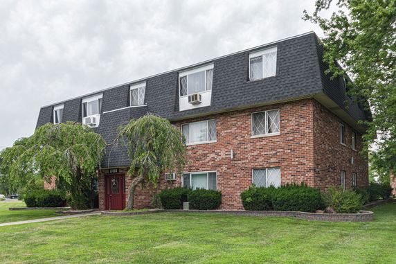 Front view of a two-story brick apartment building with a dark roof and decorative window frames.