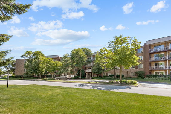 Front view of a multi-story apartment building with balconies and surrounding trees.