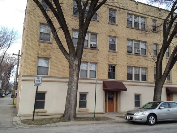 Front view of a multi-story brick building with several windows and a red awning above the entrance.