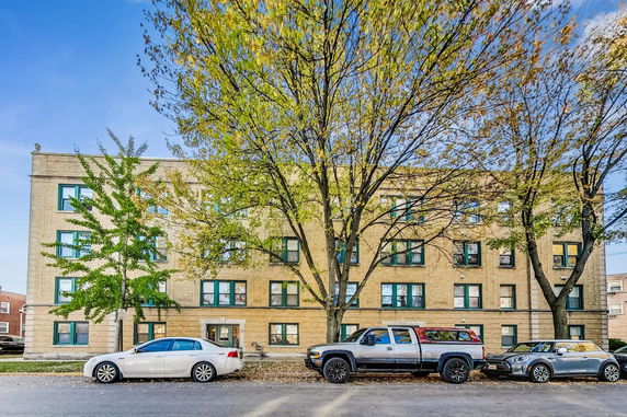 Front view of a multi-story residential building with parked cars on the street.