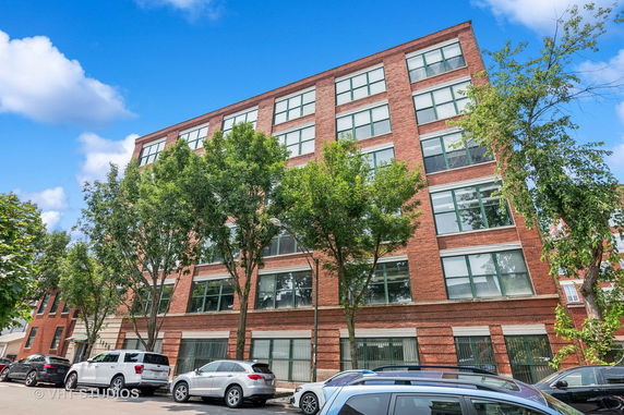 Front view of a multi-story brick building with large windows and a row of parked cars in front.