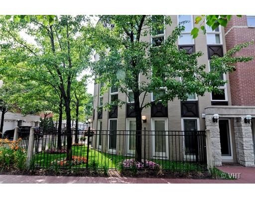Front view of a multi-story residential building with large windows and a fenced garden area.