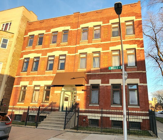 Front view of a multi-story brick building with multiple windows and an entrance staircase.