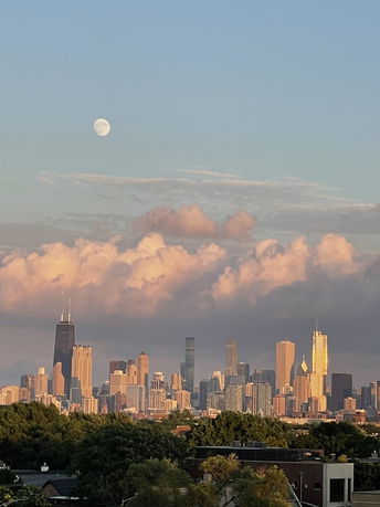 Panoramic view of a city skyline with tall buildings and a visible moon in the sky.