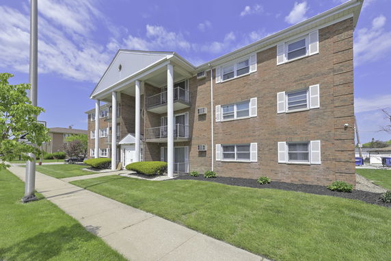 Front view of a brick three-story apartment building with balconies and white columns.
