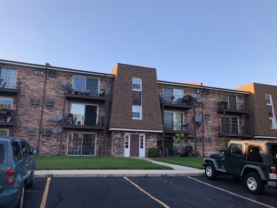 Front view of a multi-story brick apartment building with balconies and satellite dishes.