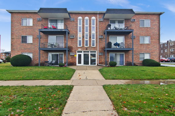 Front view of a multi-story brick apartment building with balconies.