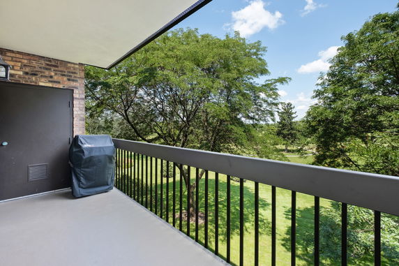 View from a balcony overlooking a green area with trees and a clear blue sky.