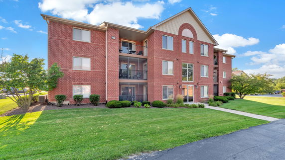 Front view of a three-story brick apartment building with balconies.