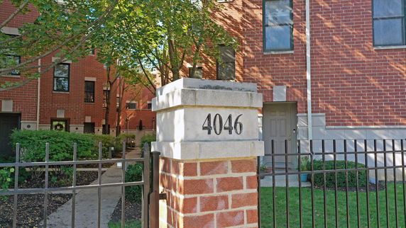 Front view of a brick building with visible door and windows, and a stone pillar marked with the number 4046.
