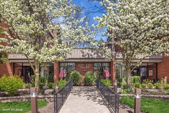 Front view of a building entrance with blooming trees and flags.