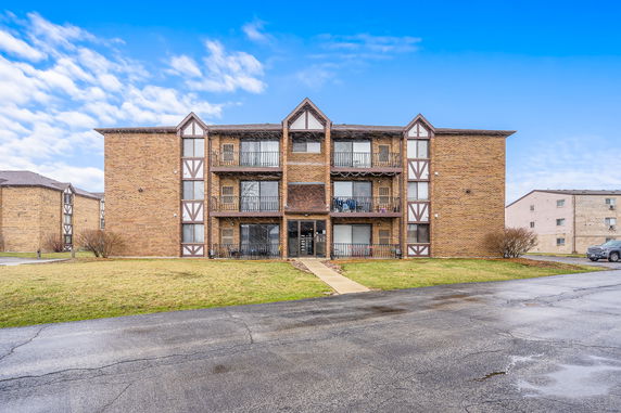Front view of a three-story brick apartment building with decorative truss elements.