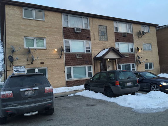 Front view of a multi-story apartment building with a brick exterior and several satellite dishes attached.