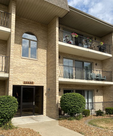 Front view of a brick apartment building with balconies and a central entrance.