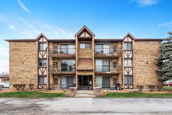Front view of a three-story brick apartment building with balconies.