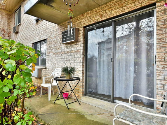 Front view of a brick building with a sliding glass door and small patio area.
