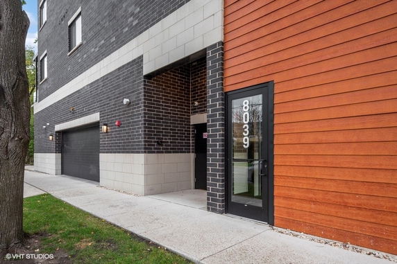Front view of a multi-story building with a modern design, featuring a combination of gray brick and wood paneling.
