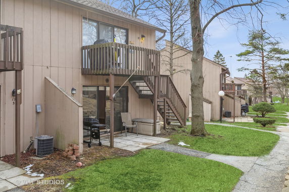 Front view of a multi-level wooden townhouse with stairs leading to an upper balcony.