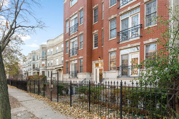 Front view of a multi-story brick residential building with iron fencing.