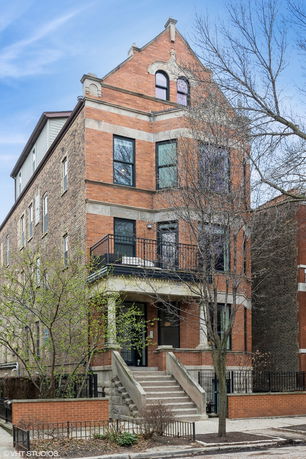 Front view of a multi-story brick house with steps leading to the entrance and a balcony.