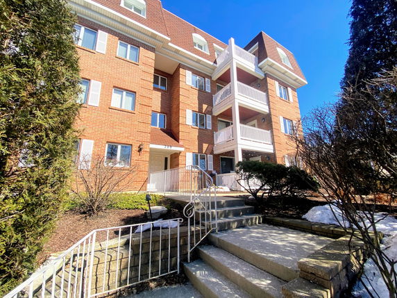 Front view of a multi-story brick apartment building with balconies and a sloped entrance.