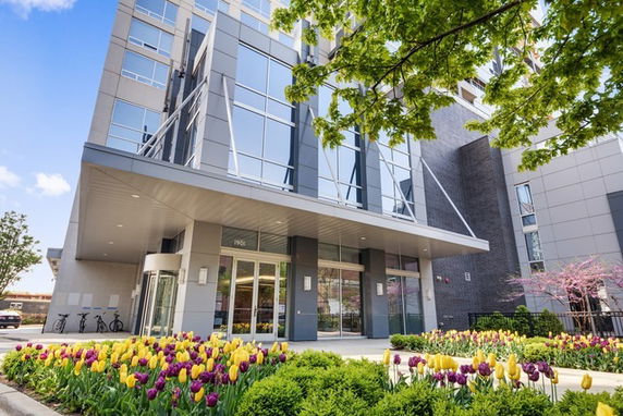 Front view of a modern multi-story building with glass windows and a landscaped entrance.