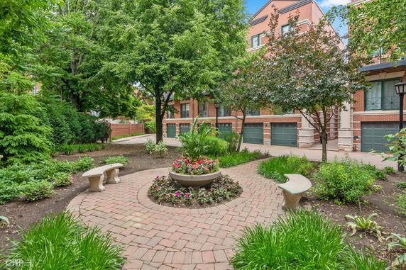 View of a landscaped outdoor area with benches and a brick building with multiple garage doors.