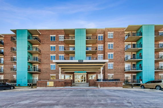 Front view of a multi-story brick apartment building with balconies and a covered entrance.