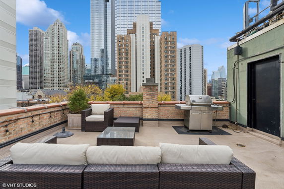 Rooftop with outdoor seating and a grill, surrounded by city buildings.