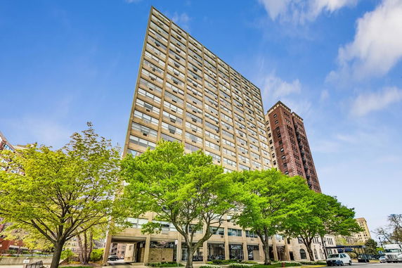 Front view of a high-rise apartment building with glass windows and a beige facade.