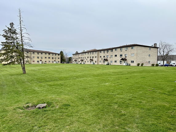 Front view of multiple three-story apartment buildings with a large grassy area in front.