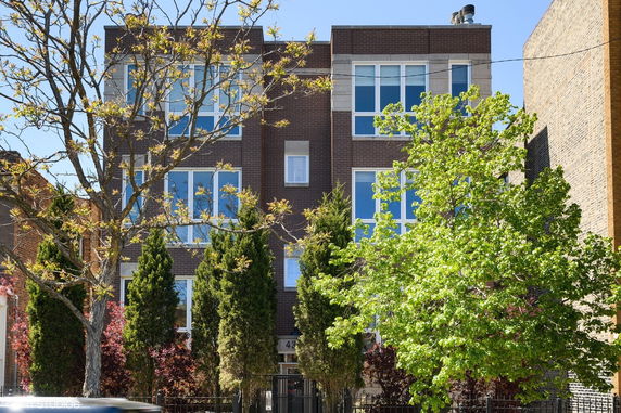 Front view of a multi-story apartment building with large windows and brick facade.