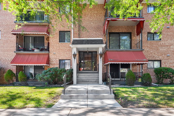Front view of a multi-story brick building with balconies and red awnings.