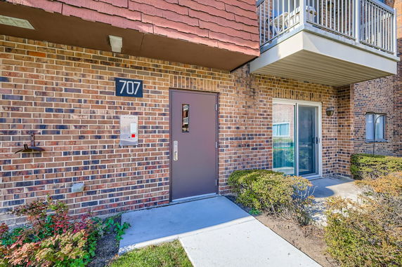 Front view of a building entrance with brick facade and balcony.