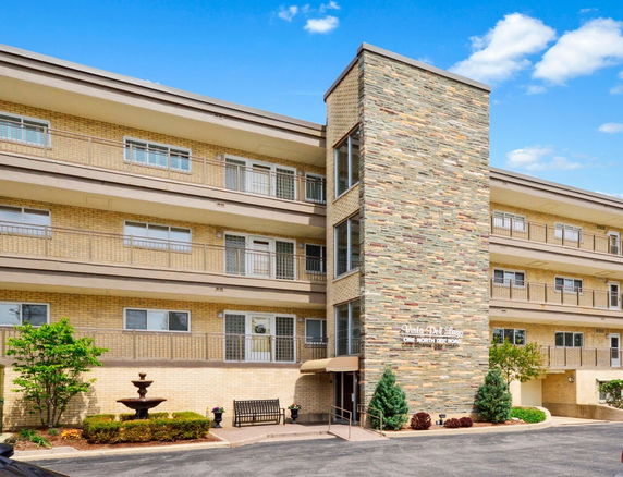 Front view of a multi-story brick building with balconies and a central elevator shaft.