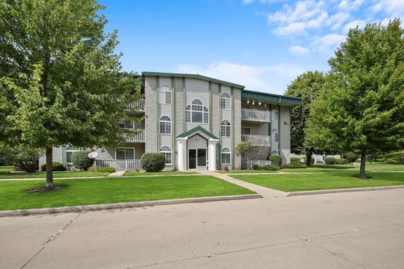 Front view of a multi-story apartment building with balconies and a green roof.