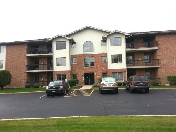Front view of a multi-story apartment building with balconies and a parking area.
